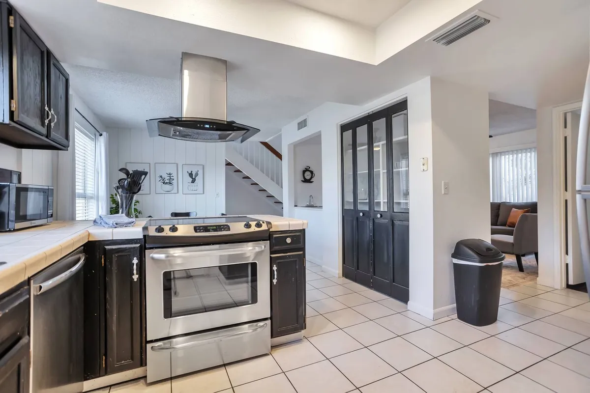 A well-equipped kitchen with stainless steel appliances, black cabinetry, ample counter space, and a view of the staircase. The area is designed for cooking, casual dining, and entertaining, making it a practical hub for groups or corporate stays.