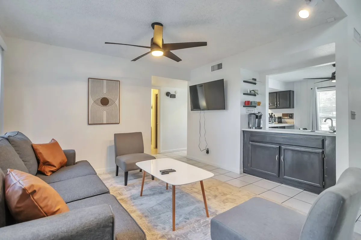 This photo spotlights a cozy living room with a gray sofa, coffee table, wall artwork, and a prominent TV, all bathed in soft natural light. The arrangement invites relaxation and togetherness, whether for catching up after a busy day or enjoying movie nights with loved ones.