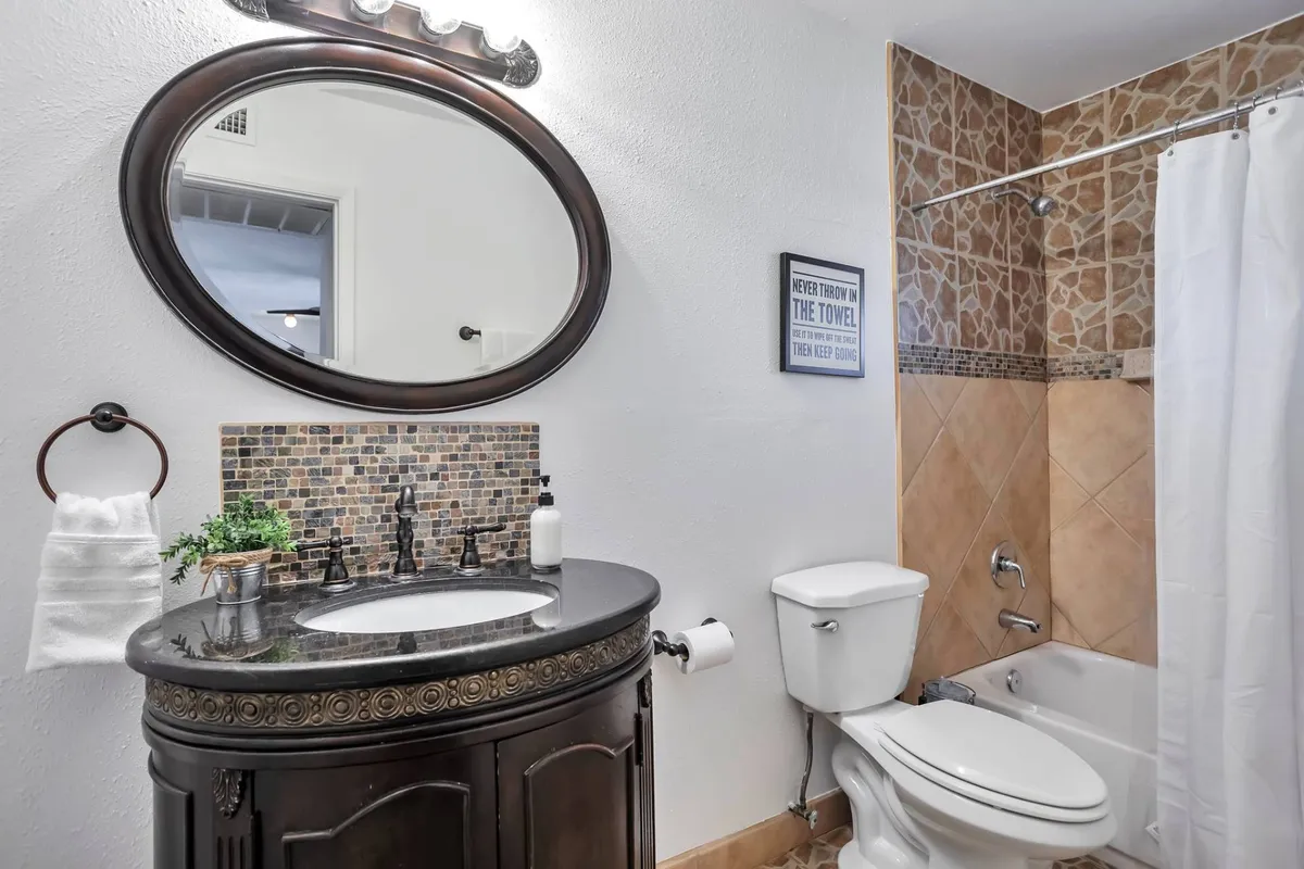 A modern bathroom featuring a double sink with dark countertops, an oval mirror, and a decorative tiled backsplash. The setup is clean, functional, and thoughtfully designed for shared use.