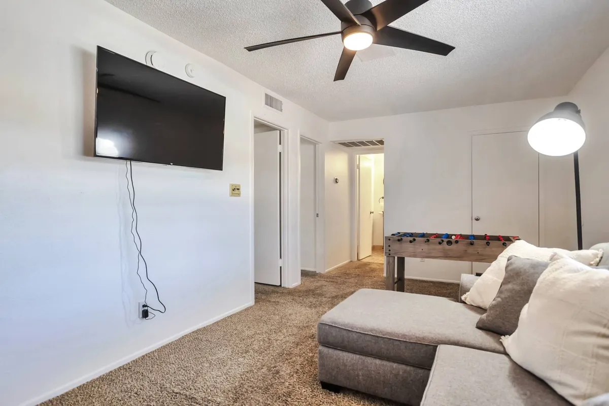 This image depicts a comfortable living area featuring a plush sofa, a large television, and a foosball table. The space is well-lit with a floor lamp and is arranged to invite group relaxation and shared activities, like watching movies or playing games together.