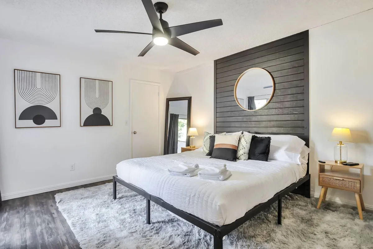 A serene guest bedroom with a plush queen bed, wall art, a mirror, nightstand, and a soft, ambient light fixture. The space exudes tranquility and comfort, ideal for restful nights.