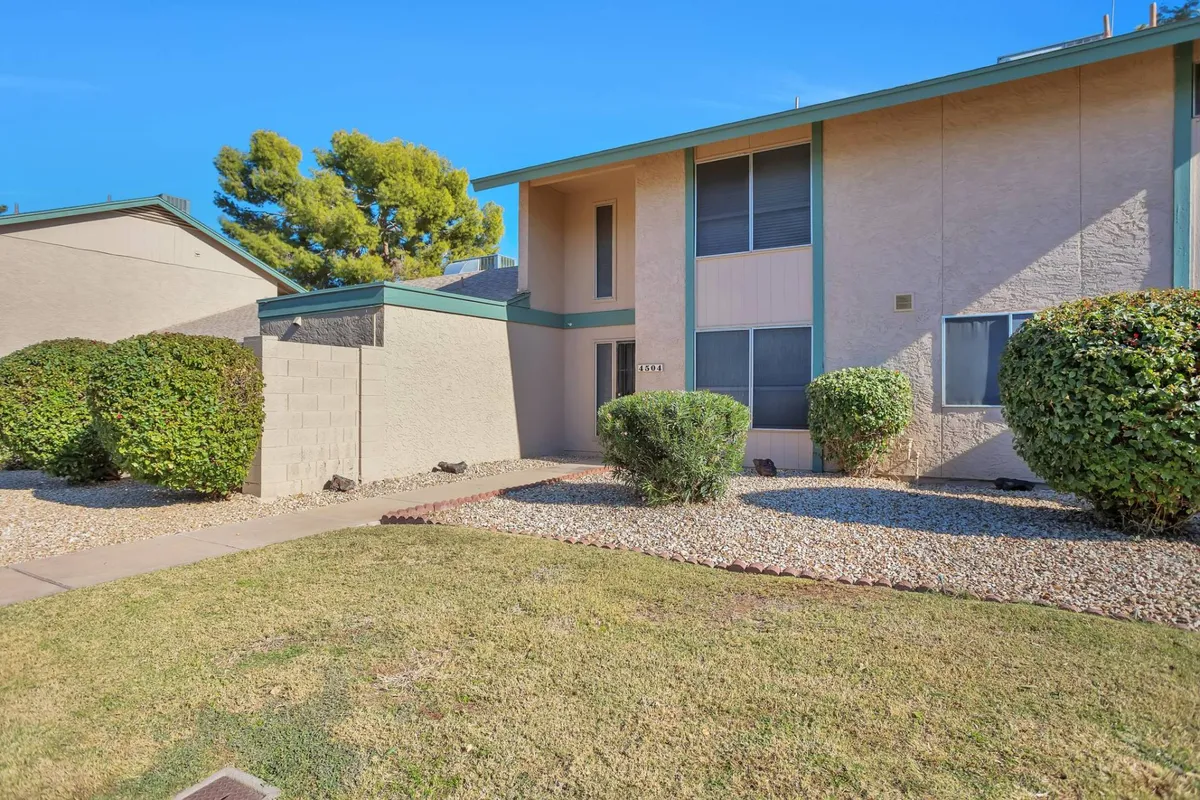 A welcoming exterior shot of the property’s front entrance with landscaped bushes, a gravel pathway, and a clear view of available parking areas, conveying easy arrival and guest parking options.