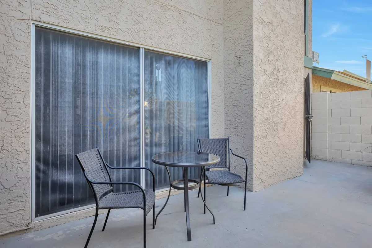 A relaxed patio scene featuring a small round table and two chairs set next to a sliding glass door, offering a seamless connection between the interior master suite and a peaceful outdoor space. The setting is ideal for enjoying coffee or quiet moments.