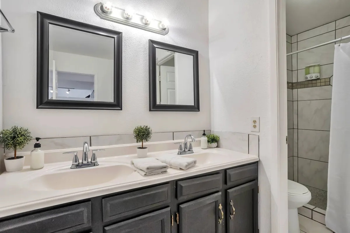 A bright, modern bathroom with double sinks, large mirrors, fresh towels, and touches of greenery. The clean lines and ample counter space evoke a refreshing, spa-like atmosphere ideal for shared use and morning routines.