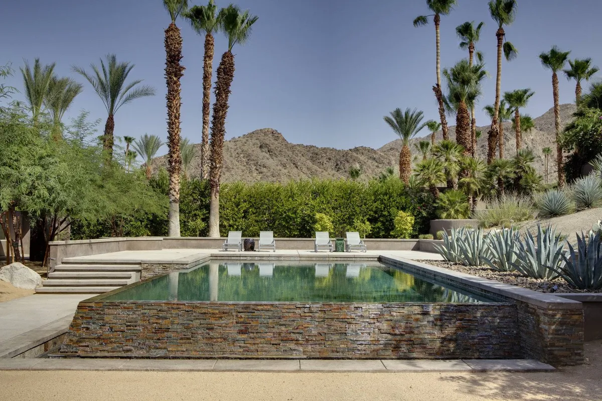 A sparkling swimming pool bordered by palm trees, inviting lounge chairs, and a scenic mountain backdrop. The area is spacious, perfect for relaxing after a day of sports or hosting an outdoor gathering. Warm lighting and a serene atmosphere suggest an ideal spot for both unwinding and socializing.