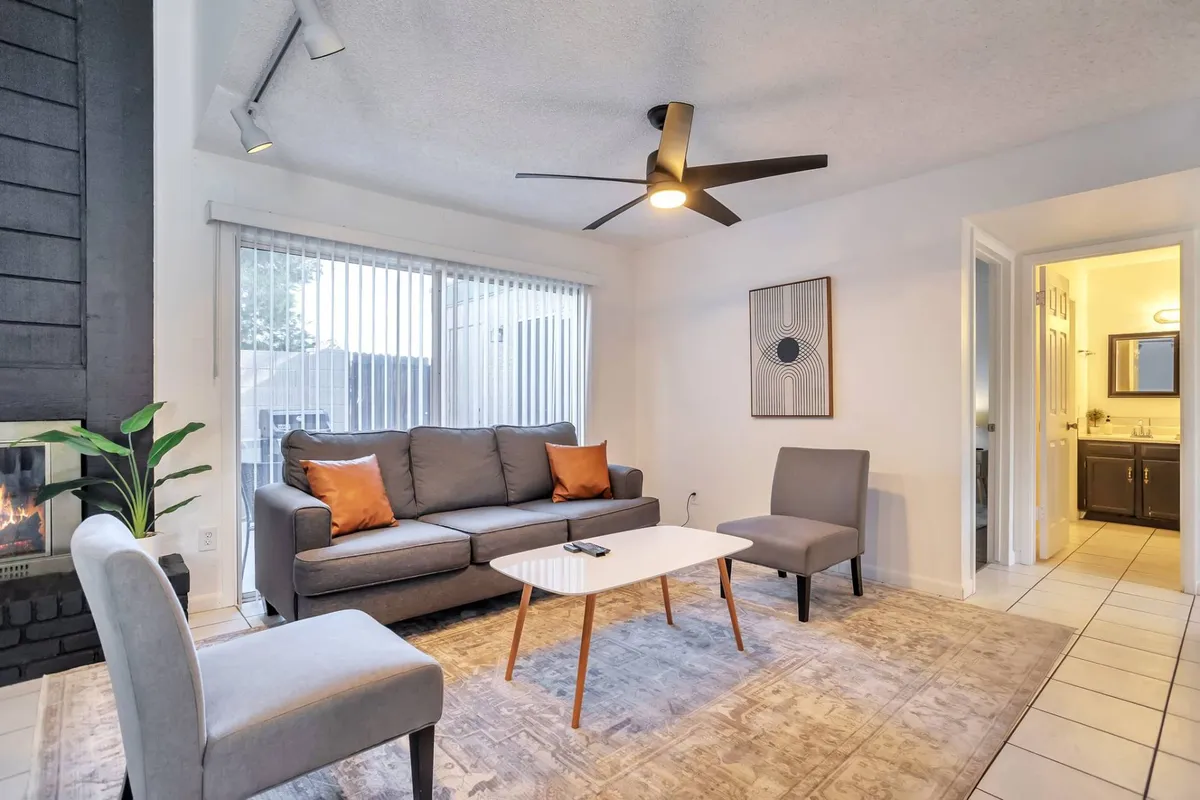 The image showcases a warm and inviting living room with a plush sofa, modern coffee table, and a glowing fireplace complemented by tasteful artwork and a ceiling fan. The ambiance is cozy and perfect for gathering, relaxing, or unwinding after a day exploring Glendale.