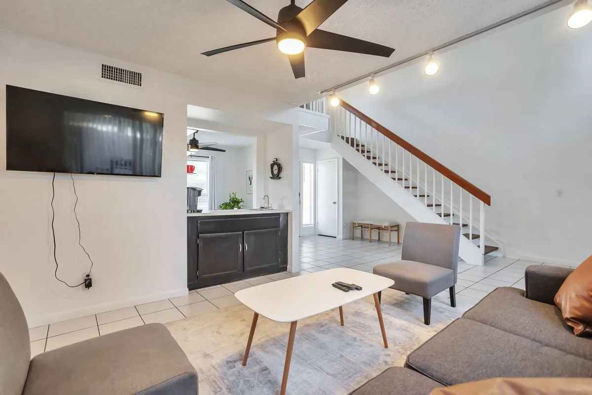 This image showcases a comfortable living area featuring a sofa, coffee table, and television, with a staircase visible in the background. The space is set up for relaxation and informal gatherings, suggesting a welcoming atmosphere after a busy day.